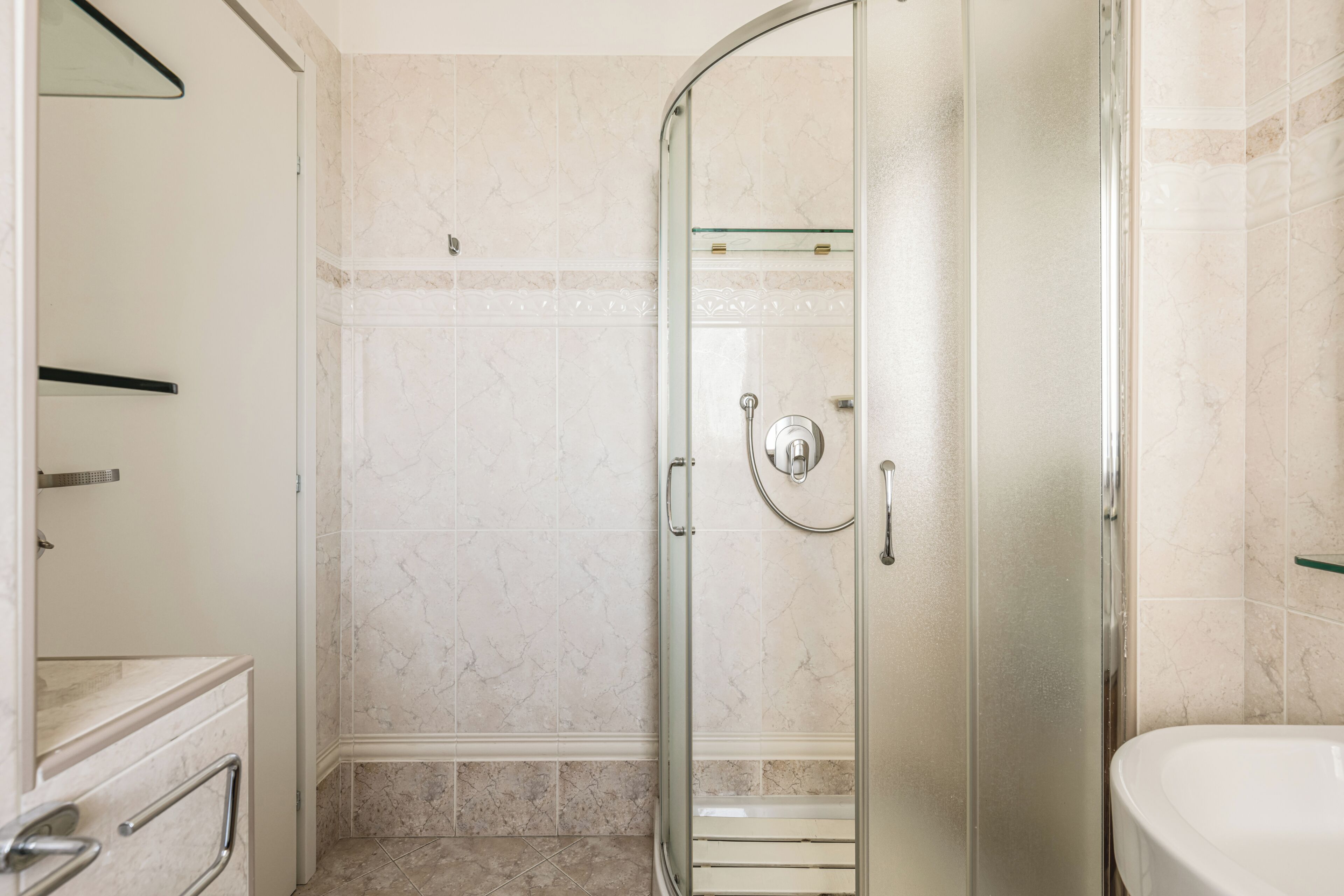 A bathroom with a glass-enclosed shower, a white sink, and a marble-tiled wall.