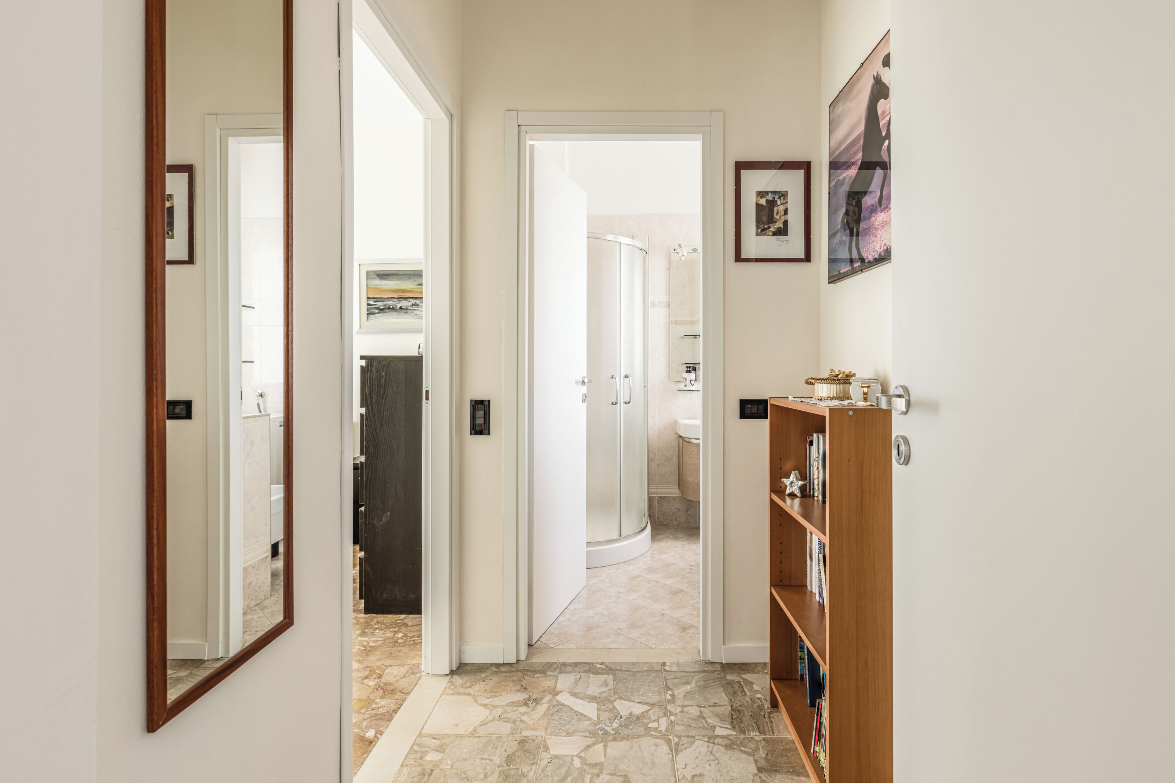 Un pasillo con un espejo, una estantería de madera y una puerta que da a un baño.
