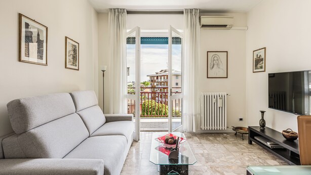 Una sala de estar con un sofá, una mesa de centro de vidrio, un televisor y vistas a través de un amplio ventanal.
