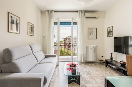 Un salon avec un canapé, une table basse en verre, un téléviseur et une vue dégagée sur l’extérieur grâce à une grande fenêtre.. Casa Vacanze Maristella