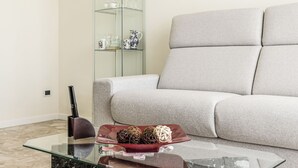 Una sala de estar con una mesa de centro de vidrio, un sofá color beige y un aparador de vidrio con objetos decorativos.