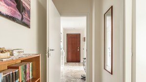 Un pasillo con una estantería, una puerta de madera y suelo de baldosas.