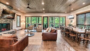 Un salón espacioso con chimenea de piedra, ventanas amplias y una zona de comedor con muebles de madera.