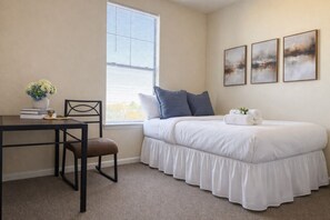 Een slaapkamer met een bed, een bureau, een stoel, een raam en drie aan de muur hangende schilderijen.
