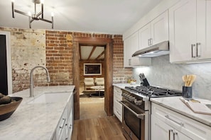 A kitchen with a brick wall, white cabinets, a gas stove, and a marble countertop. - Preserved 1800s 3BR Home, Downtown Savannah (Savannah)