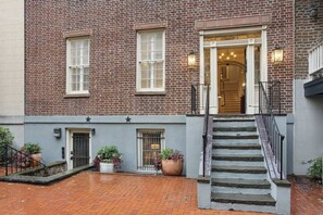 A brick building with a staircase leading to a door, potted plants, and a small outdoor area. - Preserved 1800s 3BR Home, Downtown Savannah (Savannah)