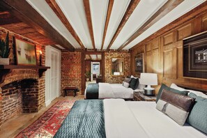 A room with exposed wooden beams, a brick fireplace, a bed with a quilted bedspread, a nightstand with a lamp, and a framed picture on the wall. - Preserved 1800s 3BR Home, Downtown Savannah (Savannah)