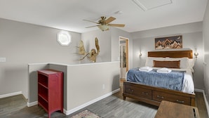 Ein Schlafzimmer mit einem Bett, einem Deckenventilator, einem roten Regal, einem Nachttisch aus Holz und einem Bild an der Wand.