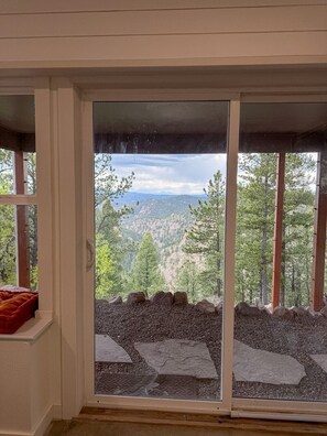 A room with a large sliding glass door leading to a scenic outdoor view of a forested mountain range. - Sunset Ridge Escape with Hot Tub & Incredible Mountain Views (Divide)