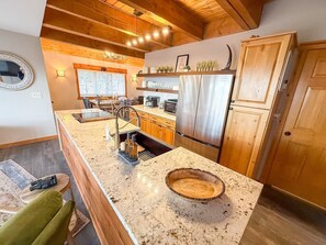 A kitchen with granite countertops, stainless steel appliances, wooden cabinets, and a wooden dining table with chairs. - Sunset Ridge Escape with Hot Tub & Incredible Mountain Views (Divide)