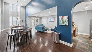 Une pièce spacieuse comprenant un coin repas, des canapés bleus et des œuvres d’art accrochées aux murs.