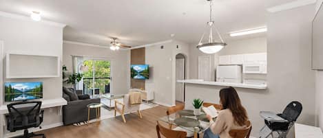 A modern living room with a dining area, a TV mounted on the wall, and a ceiling fan.