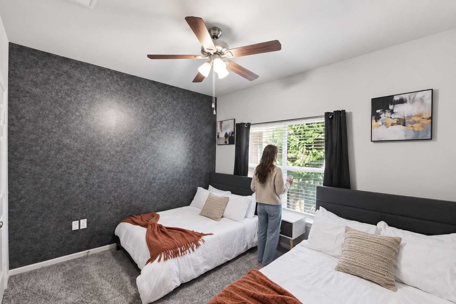 Una habitación de hotel moderna con dos camas, un ventilador de techo, un ventanal con cortinas y un cuadro en la pared.