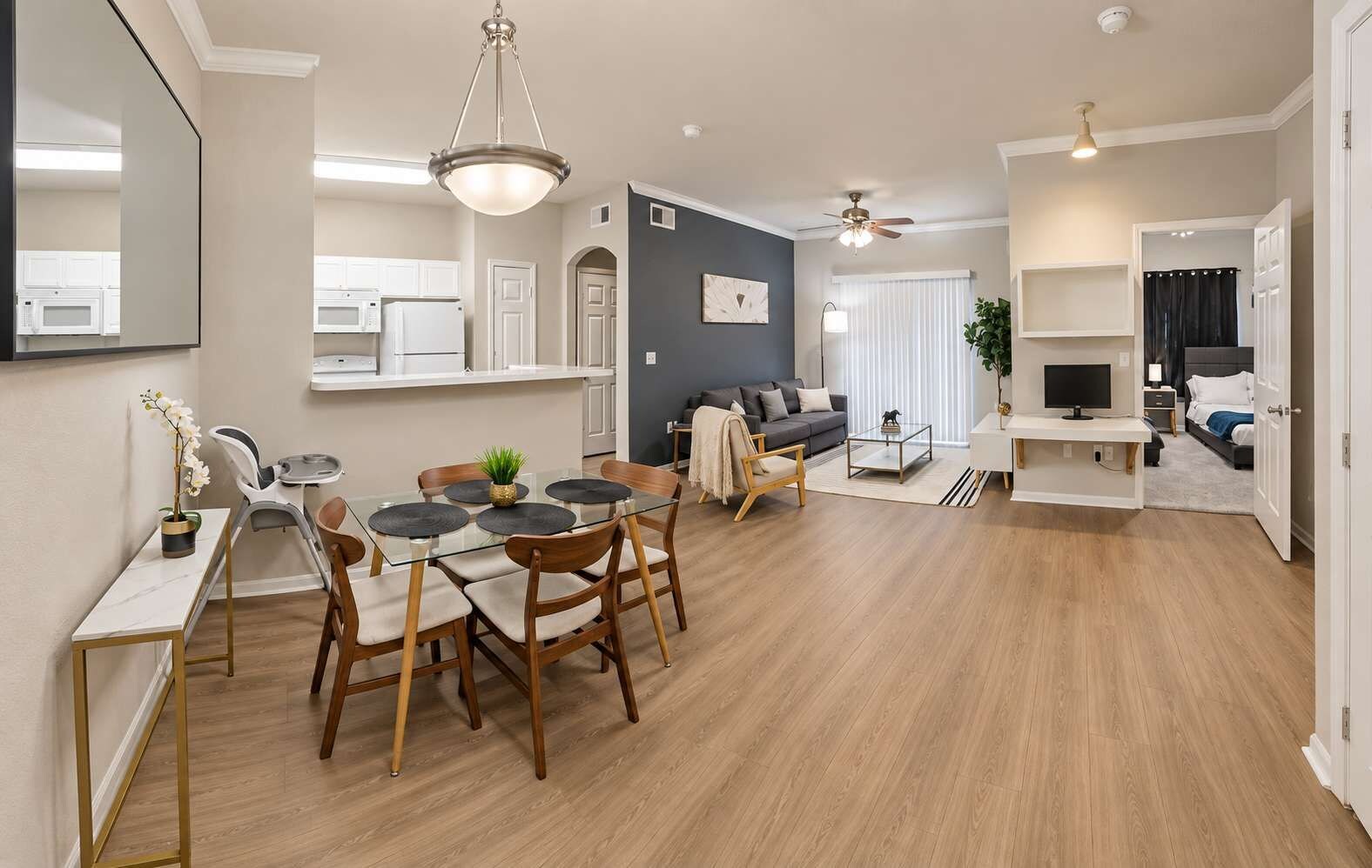 A modern living space with a dining area, a sofa, a TV, and a kitchen in the background.