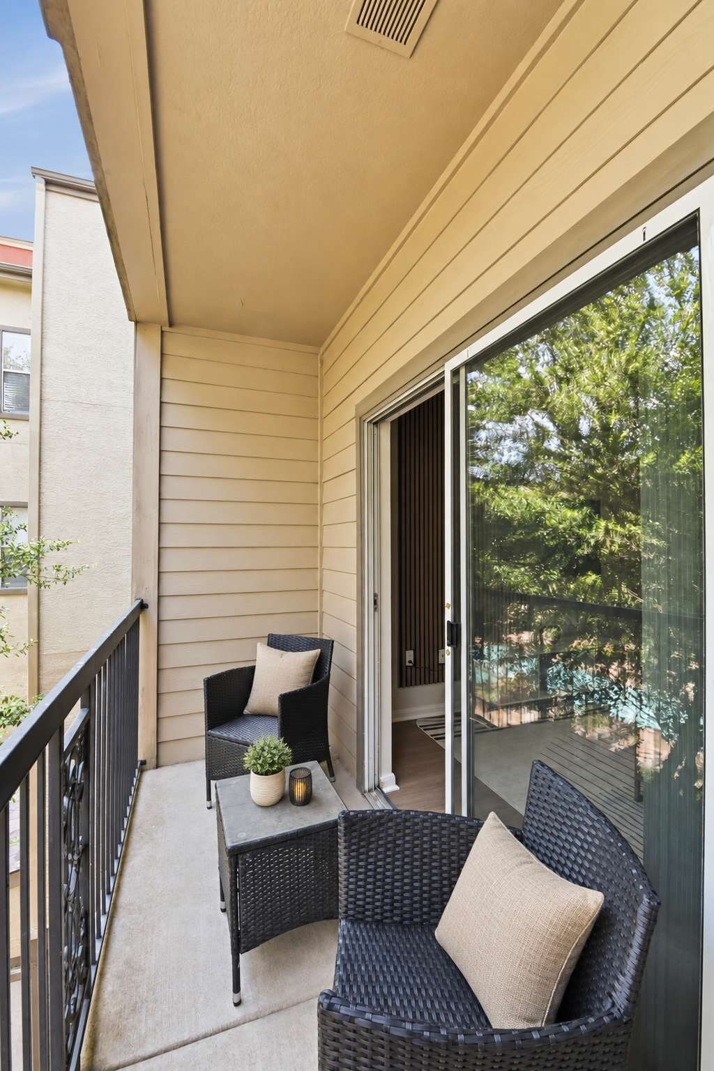 A balcony with two wicker chairs, a small table, and a potted plant.