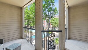 Ein Balkon mit Blick auf ein Schwimmbad und Bäume, einem Metallgeländer und einem Korbstuhl.