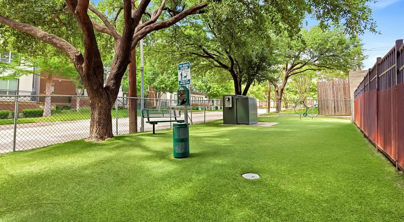 A fenced outdoor area with a pet waste station, a bench, and a trash bin.