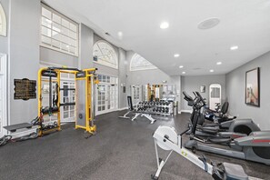 Ein Fitnessraum mit Trainingsgeräten, einem Schild mit Notfallhinweisen und großen Fenstern.