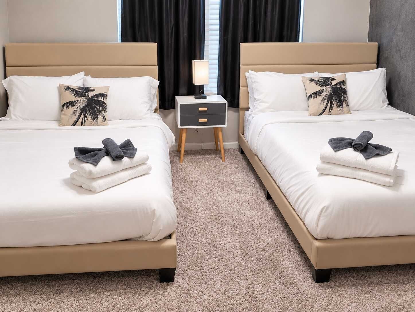 A hotel room with two beds, each with a pillow, a bedside table with a lamp, and towels.
