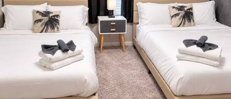 A hotel room with two beds, each with a pillow, a bedside table with a lamp, and towels.