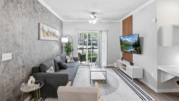 A modern living room with a grey sofa, a glass coffee table, a TV mounted on the wall, and a view of the outdoors through large windows. - Modern Dallas Stay Near Love Field and Pool (Dallas)