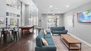 Amplia habitación con mesa de billar, asientos de bar, sofá y televisor en la pared.