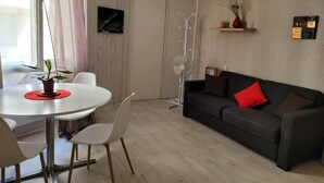 A modern living room with a dining table, chairs, a sofa, and a standing fan.