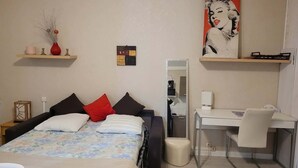 A bedroom with a bed, a desk, a chair, a mirror, and a painting on the wall.