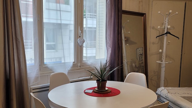 A room with a round table, four chairs, a potted plant, a coat rack, and a bed.