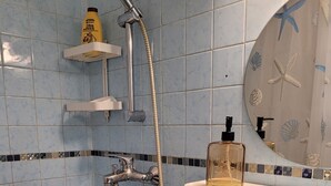 A bathroom with blue tiles, a shower, a sink, and a mirror with a sea-themed design.