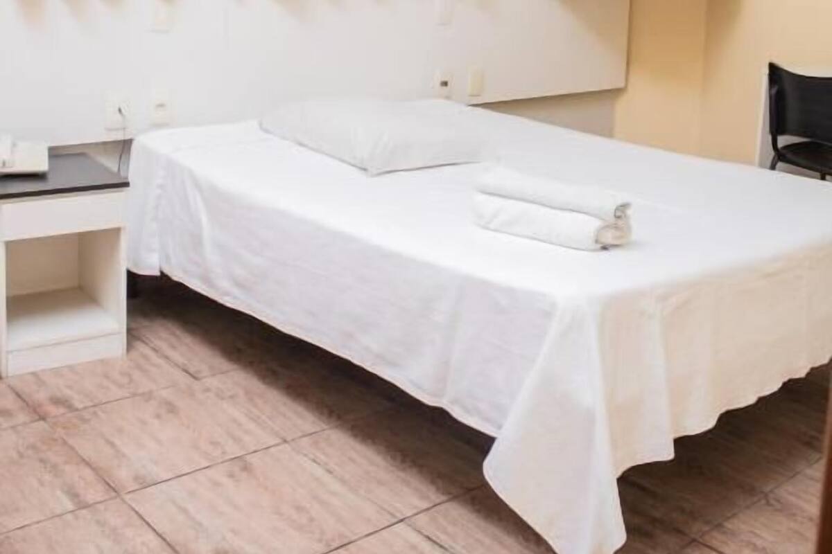 A single bed with a white bedspread and pillows, a bedside table, a chair, and a wall-mounted cabinet.