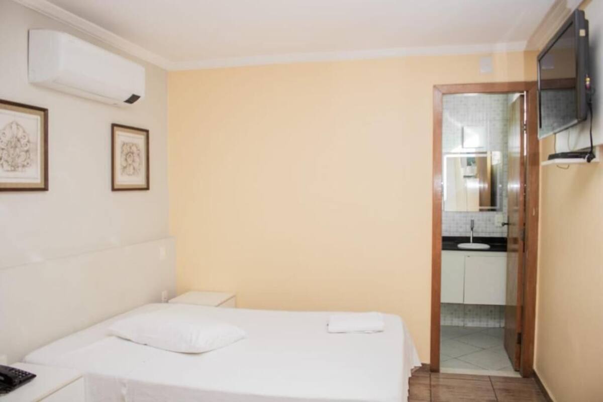 A hotel room with a bed, a bedside table, a TV mounted on the wall, and a door leading to a bathroom.