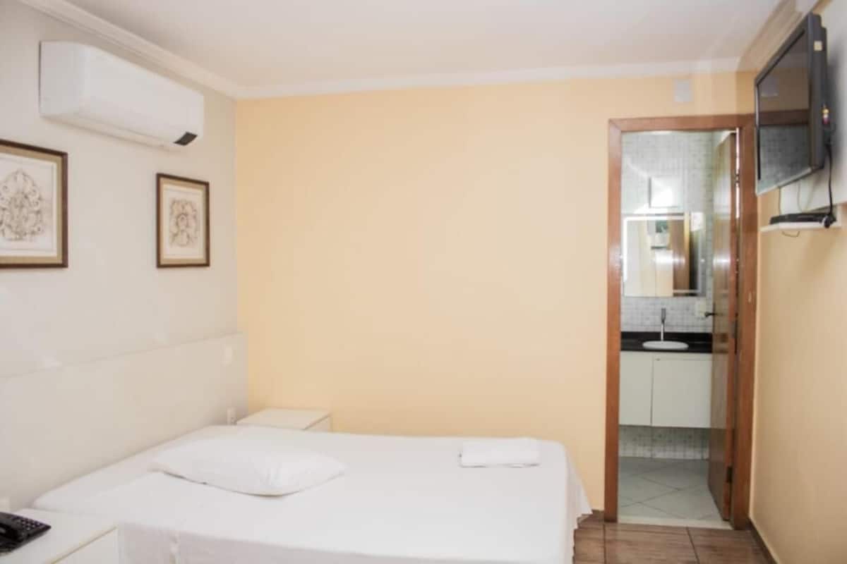 A hotel room with a bed, a bedside table, a TV mounted on the wall, and a door leading to a bathroom.