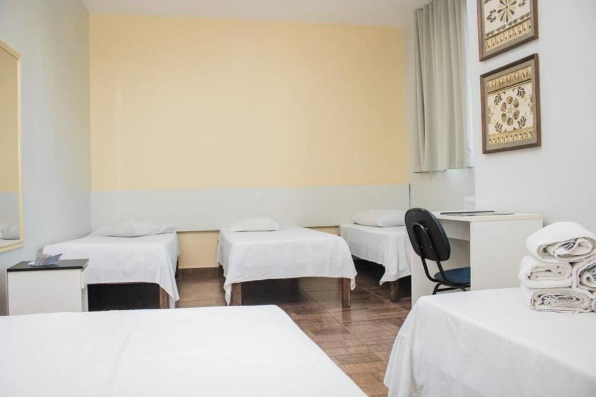 A hotel room with three beds, a desk, a chair, and a stack of towels.