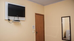 A room with a television mounted on the wall, a wooden door, and a mirror.