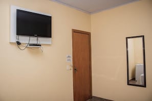 Una habitación con un televisor montado en la pared, una puerta de madera y un espejo.