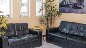 A lobby with two black leather sofas, a small yellow table, a large potted plant, and a cityscape painting on the wall.