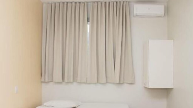 A hotel room with three beds, a window with curtains, an air conditioning unit, and a white cabinet.