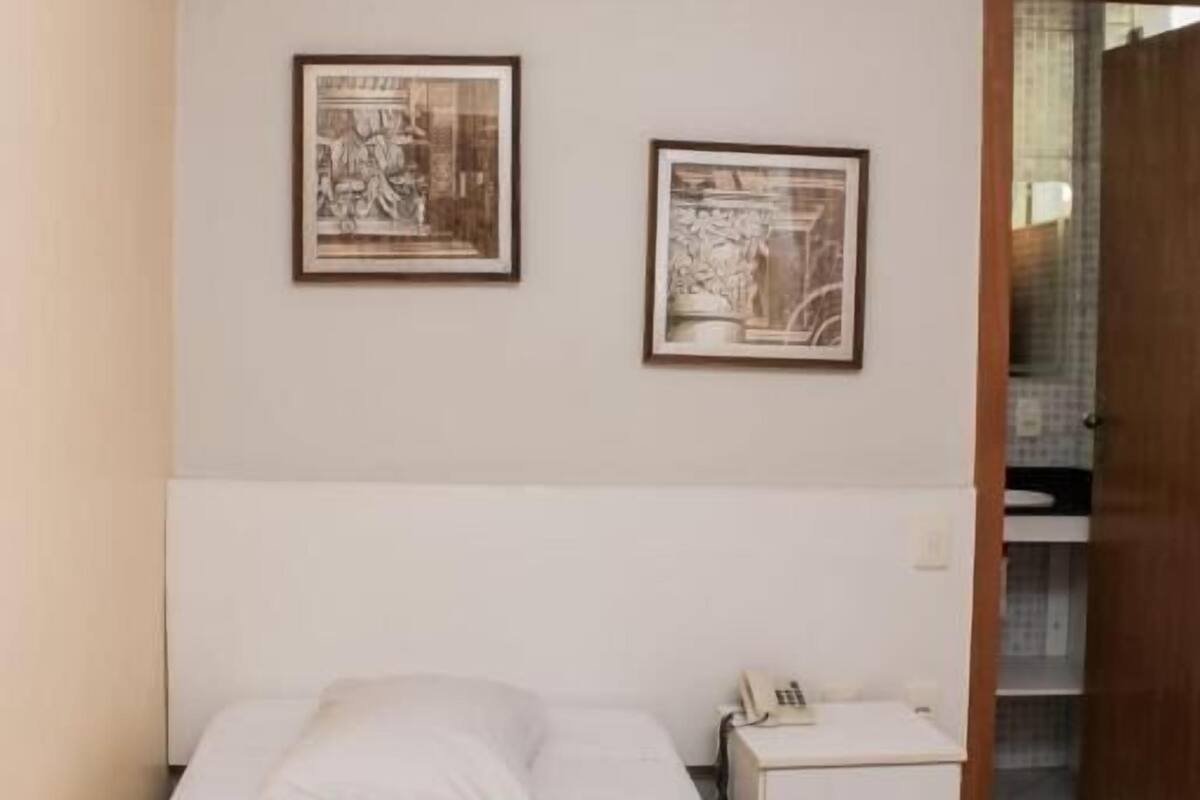 A single bed with a rolled towel, a bedside table with a phone, and two framed pictures on the wall.