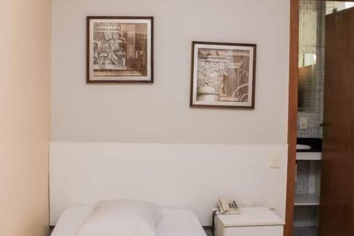 A single bed with a rolled towel, a bedside table with a phone, and two framed pictures on the wall.