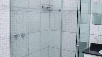 A glass-enclosed shower with a white tiled wall, a white bathtub, and a white cabinet.