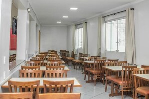 A dining area with multiple wooden tables and chairs, large windows with curtains, and a tiled floor. - Campos Gerais Hotel (Belo Horizonte)