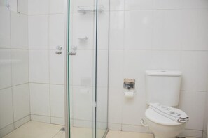 A bathroom with a glass shower enclosure, a toilet, and a small shelf. - Campos Gerais Hotel (Belo Horizonte)