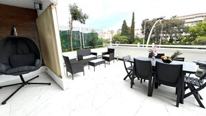 Une terrasse avec une chaise noire, des fauteuils en osier noir et une table sur laquelle se trouvent des fruits.