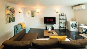 Un salon comprenant un canapé, un téléviseur, un lave-linge et un coin repas.