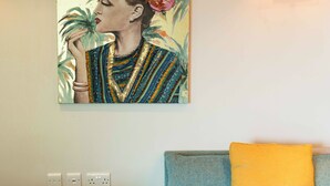 Une pièce avec un canapé bleu, un coussin jaune et un tableau accroché au mur.