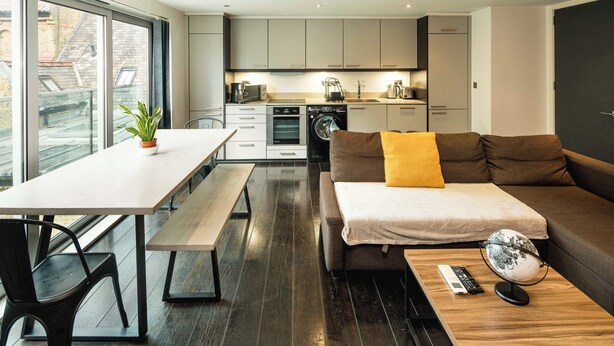 Un appartement moderne comprenant un coin repas, un canapé avec un coussin jaune, un globe terrestre et un lave-linge dans la cuisine.