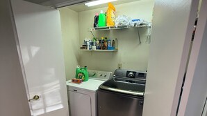 Una cocina funcional con lavadora, estufa y repisas superiores que albergan distintos utensilios de cocina.