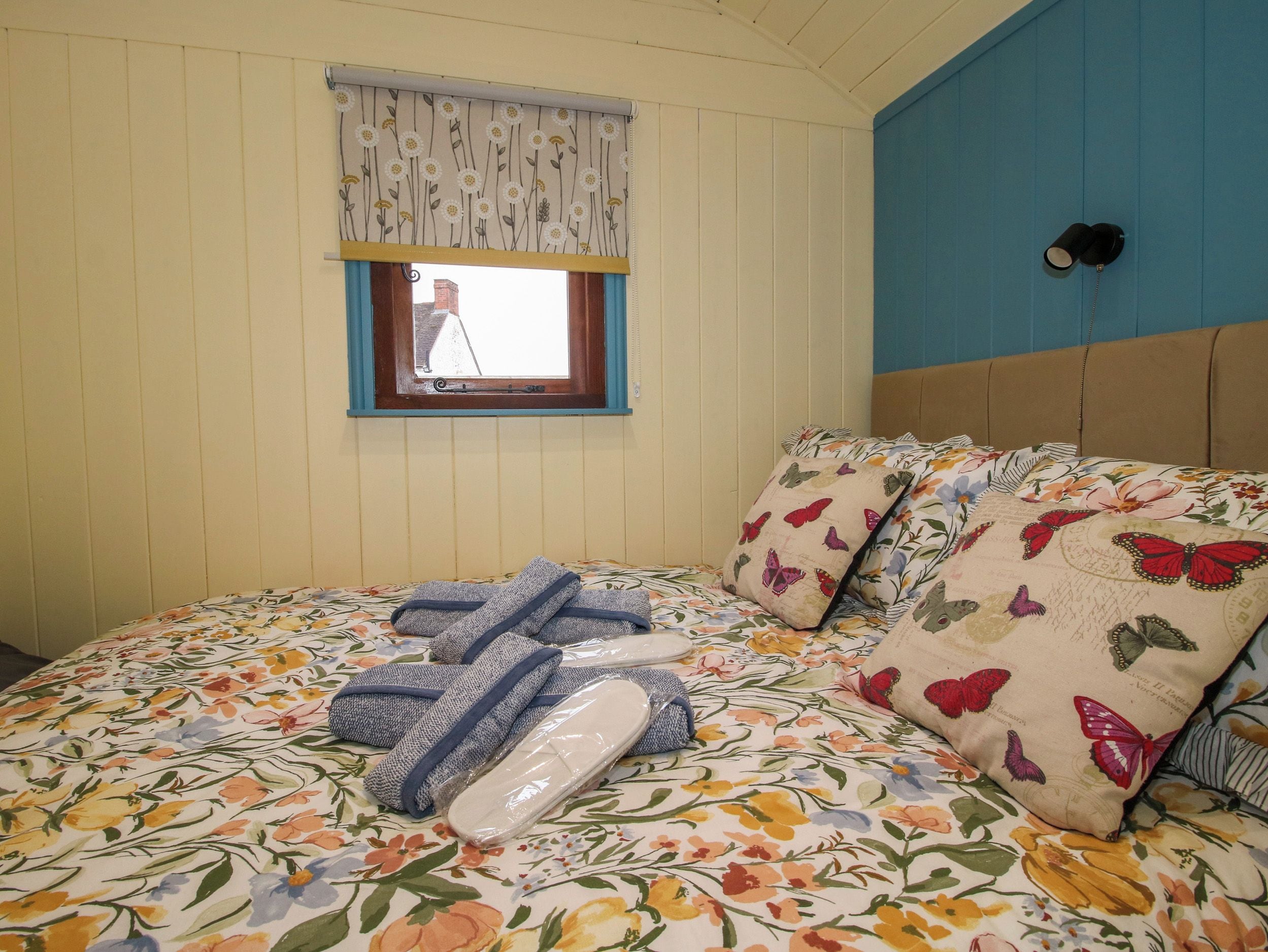A bedroom with a floral bedspread, a window with a curtain, and a bed with multiple pillows.