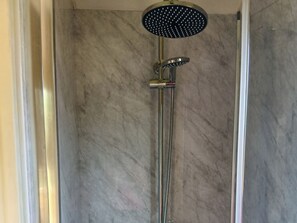 Eine Dusche mit Handbrause und wandmontiertem Wasserhahn in einem Badezimmer mit Marmorwänden.